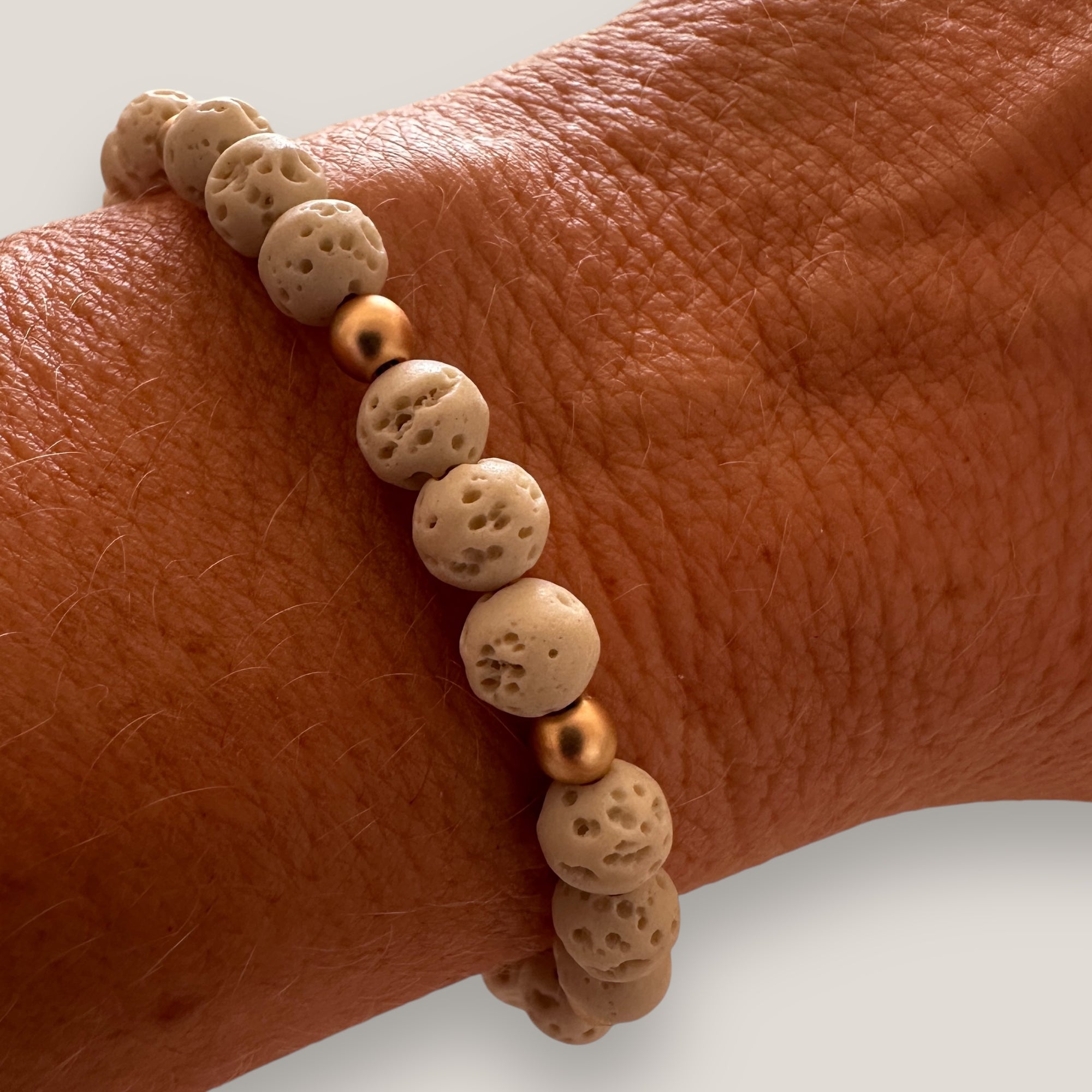 Armband auf beigefarbener Korallenschwammbasis und goldenen Hämatiten