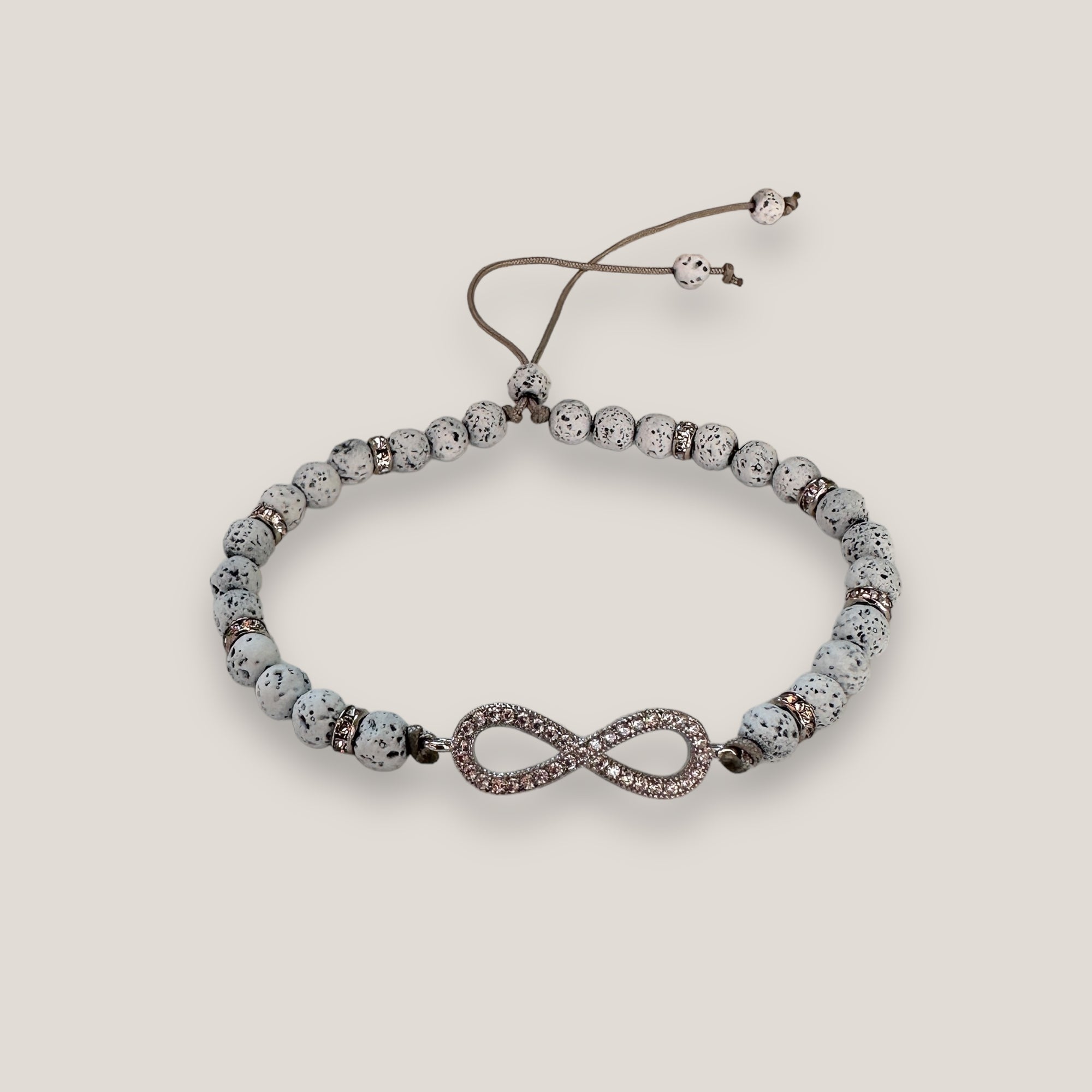 Pulsera con infiniti plateado con brillis, lava blamca y separadores con más brillis