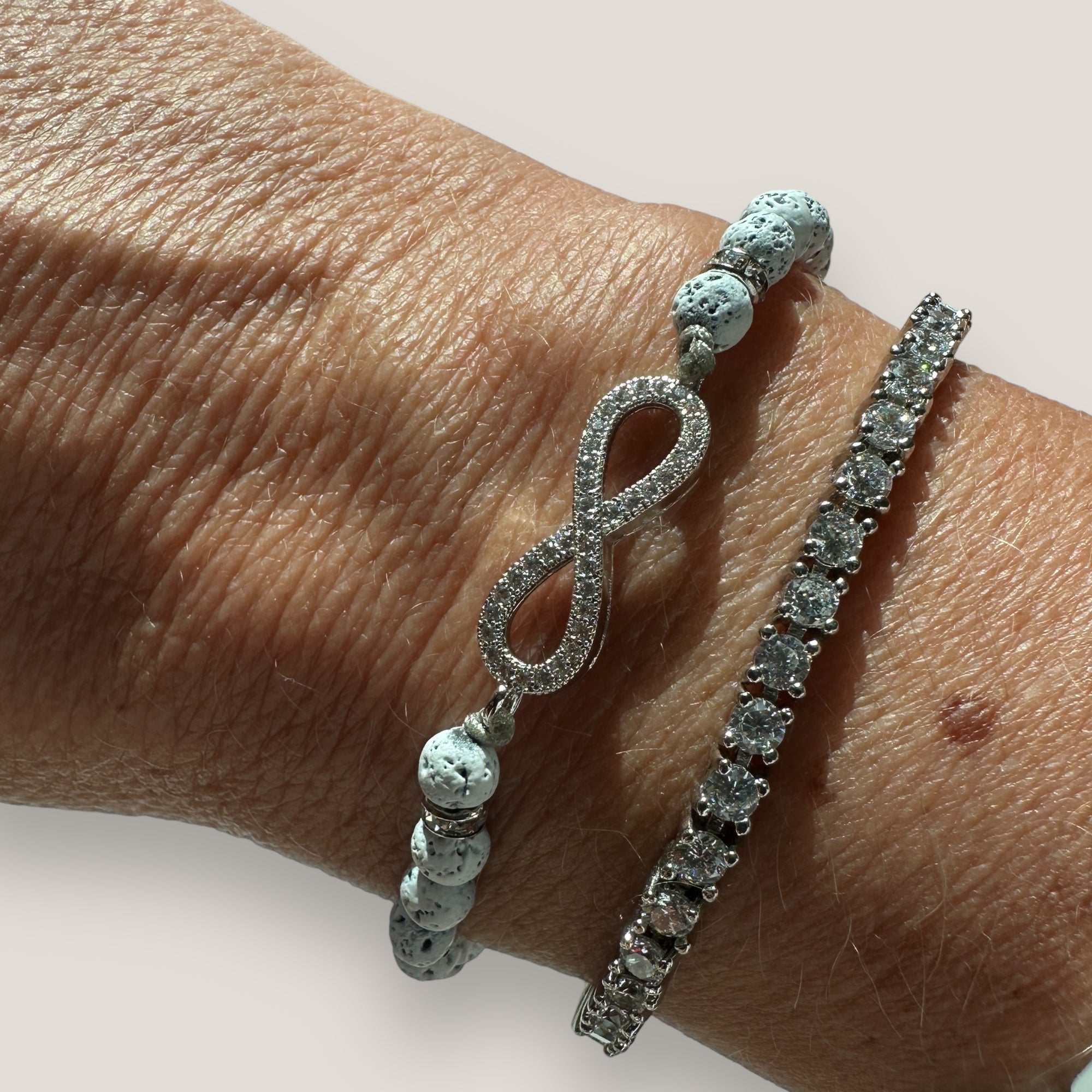 Pulsera con infiniti plateado con brillis, lava blamca y separadores con más brillis