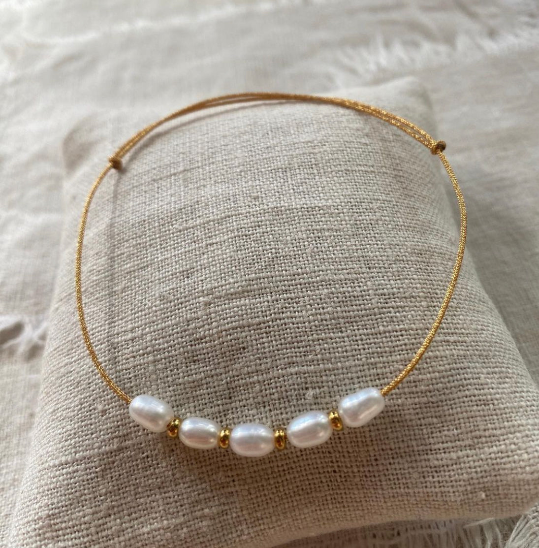Pulsera minimal con hilera de cinco perlas naturales blancas, separadores de acero oro y cordón oro con nudos correderos