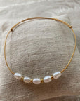 Pulsera minimal con hilera de cinco perlas naturales blancas, separadores de acero oro y cordón oro con nudos correderos