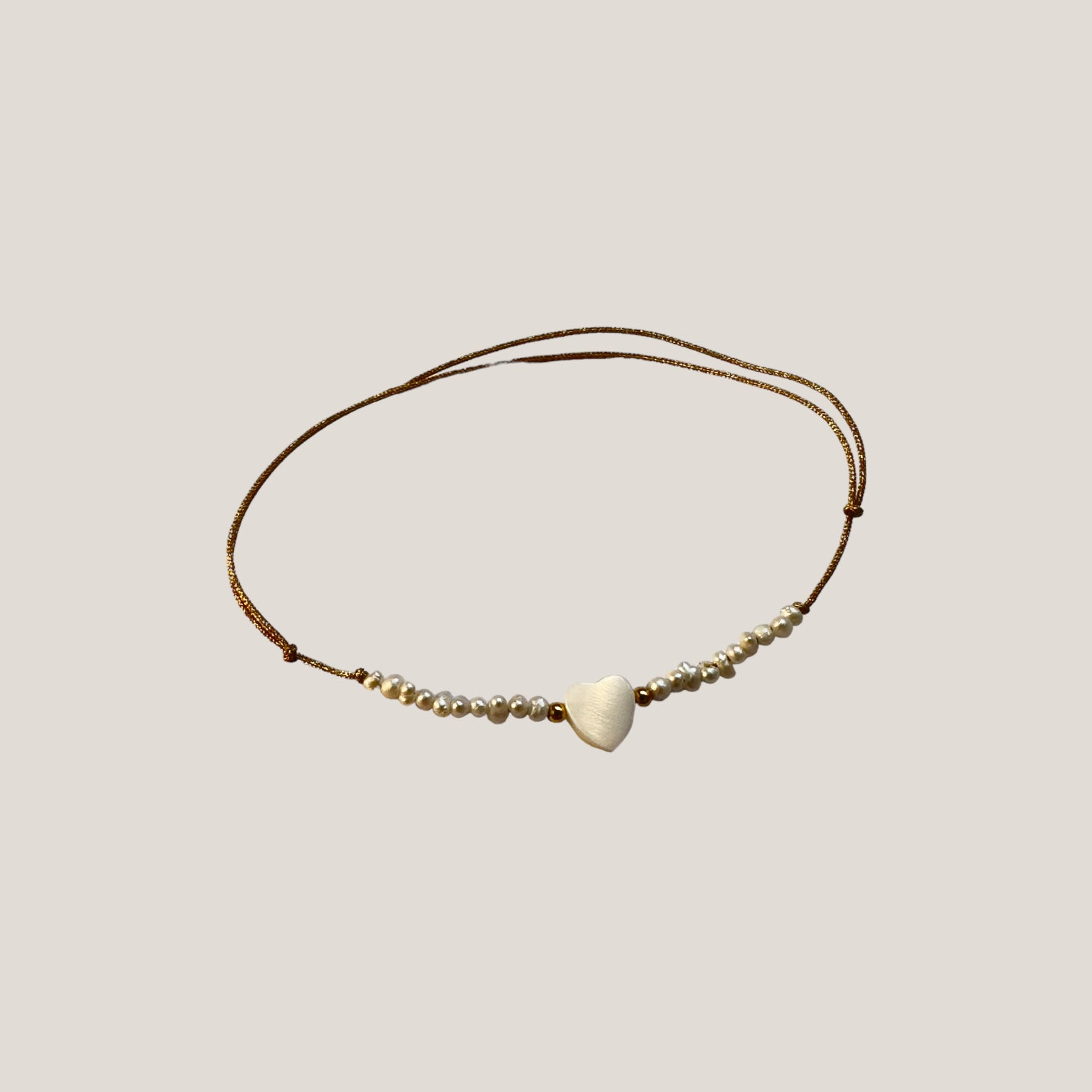 Minimalistisches Armband mit einer Reihe natürlicher Perlen, einem Perlmuttherz und einer Goldkordel mit Schiebeknoten