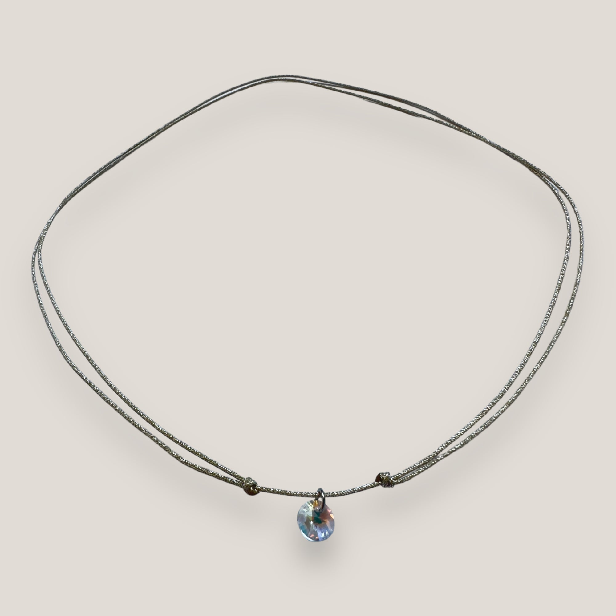 Collar minimal con cristal facetado alto brillo, cordón plata y nudos correderos