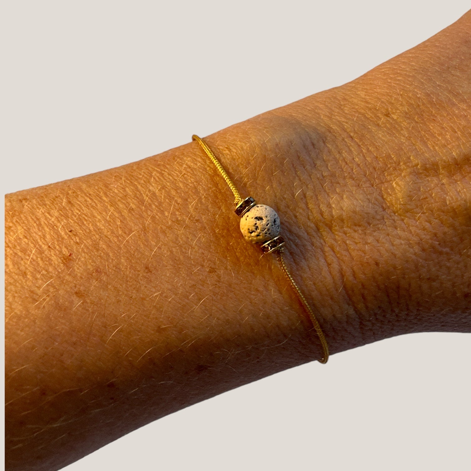 Pulsera minimal con bola de lava arena y cuentas doradas con brillis ámbar